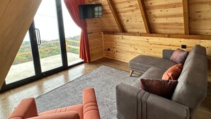 Ein gemütlicher Raum mit schrägem Dach, Holzwänden, einem grauen Sofa und einem roten Vorhang.