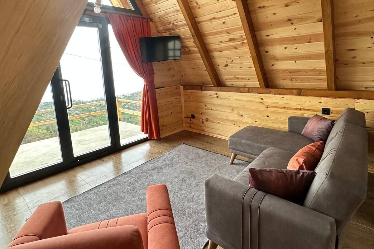 A cozy room with a sloped ceiling, wooden walls, a gray sofa, and a red curtain.