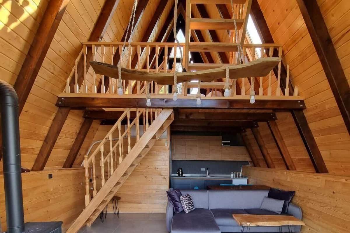 A high-ceilinged attic room with a wooden staircase, a sofa, and a wood-burning stove.