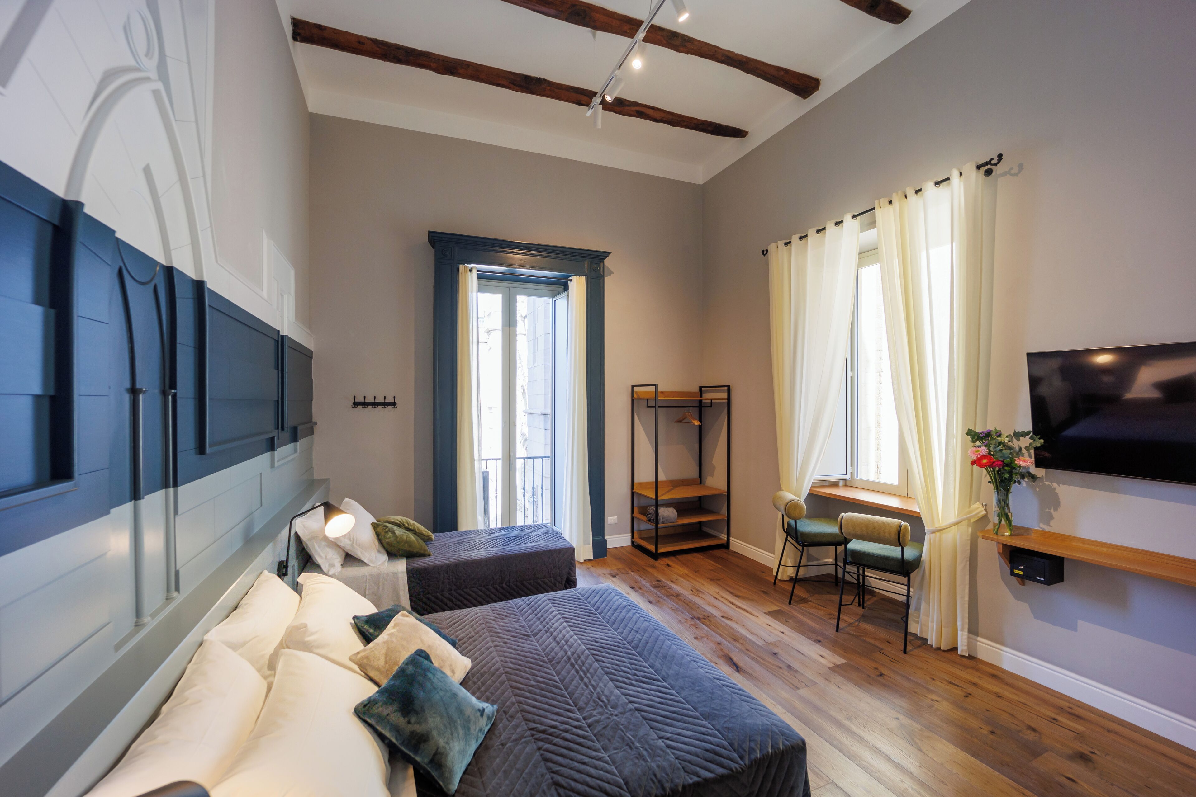 A modern bedroom with a large bed, a TV, a seating area, and a window with curtains.