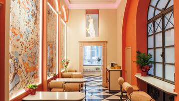 Una hall d'albergo con pavimento a scacchi, zone relax e ampie finestre ad arco.
