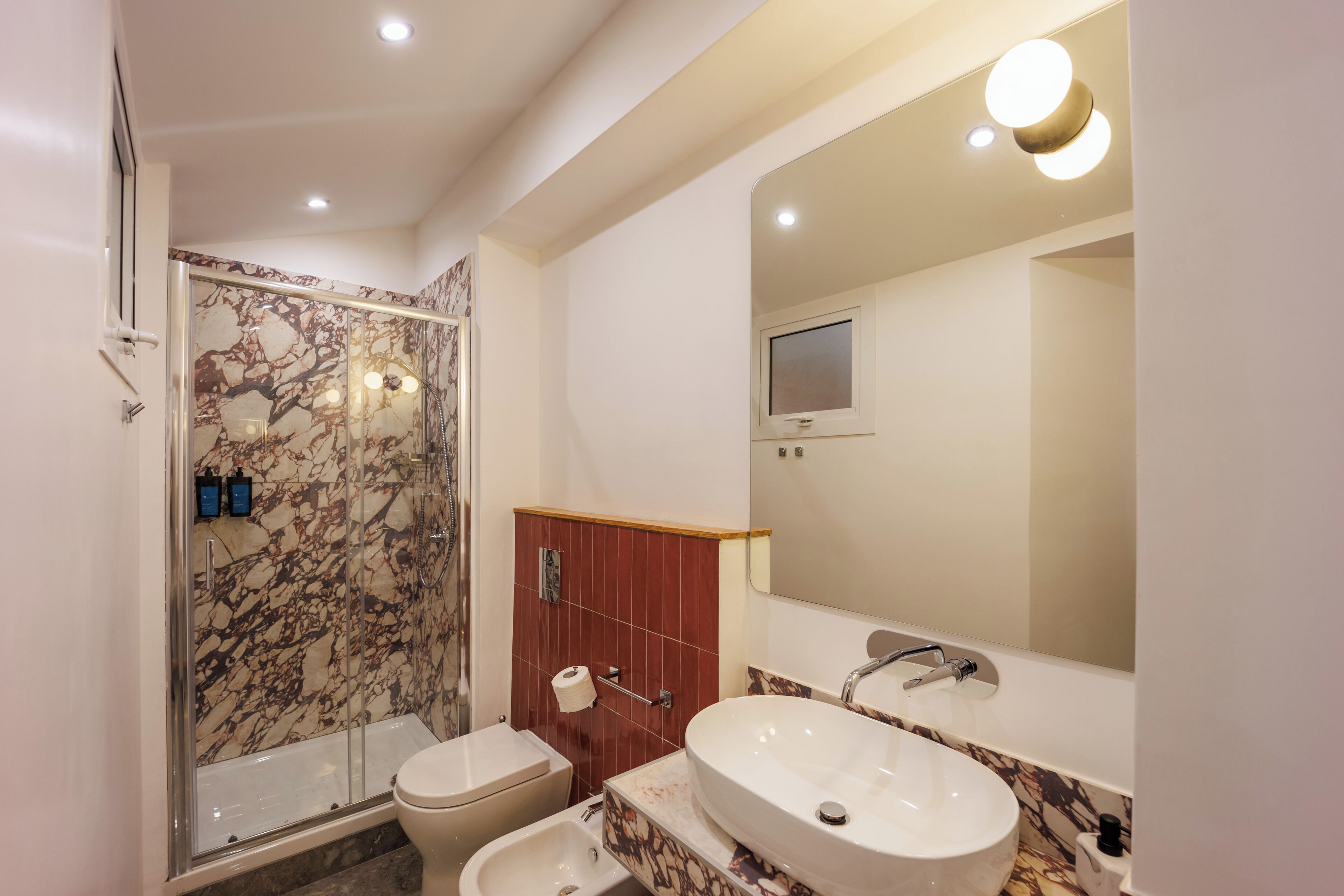 Un baño moderno con ducha envuelta en vidrio, inodoro, lavamanos y espejo.