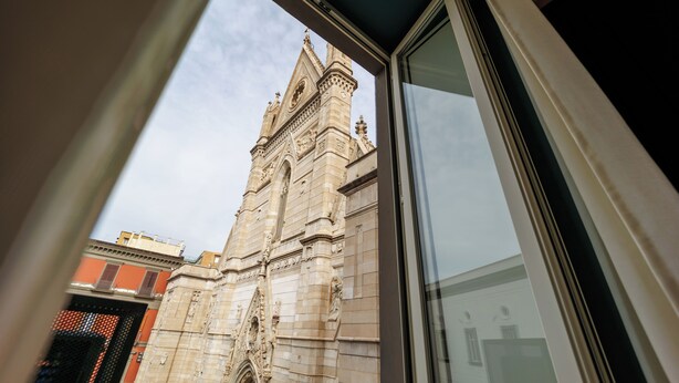 A view through a window of a building with ornate architectural details and a clock tower. - The Other Duomo House (Naples)
