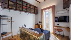 A compact bedroom with a bed, a desk, a chair, a bookshelf, and a TV. - The Other Duomo House (Naples)