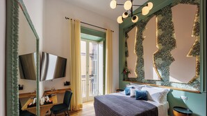 A hotel room with a bed, a desk with a chair, a television, and a large mirror. - The Other Duomo House (Naples)
