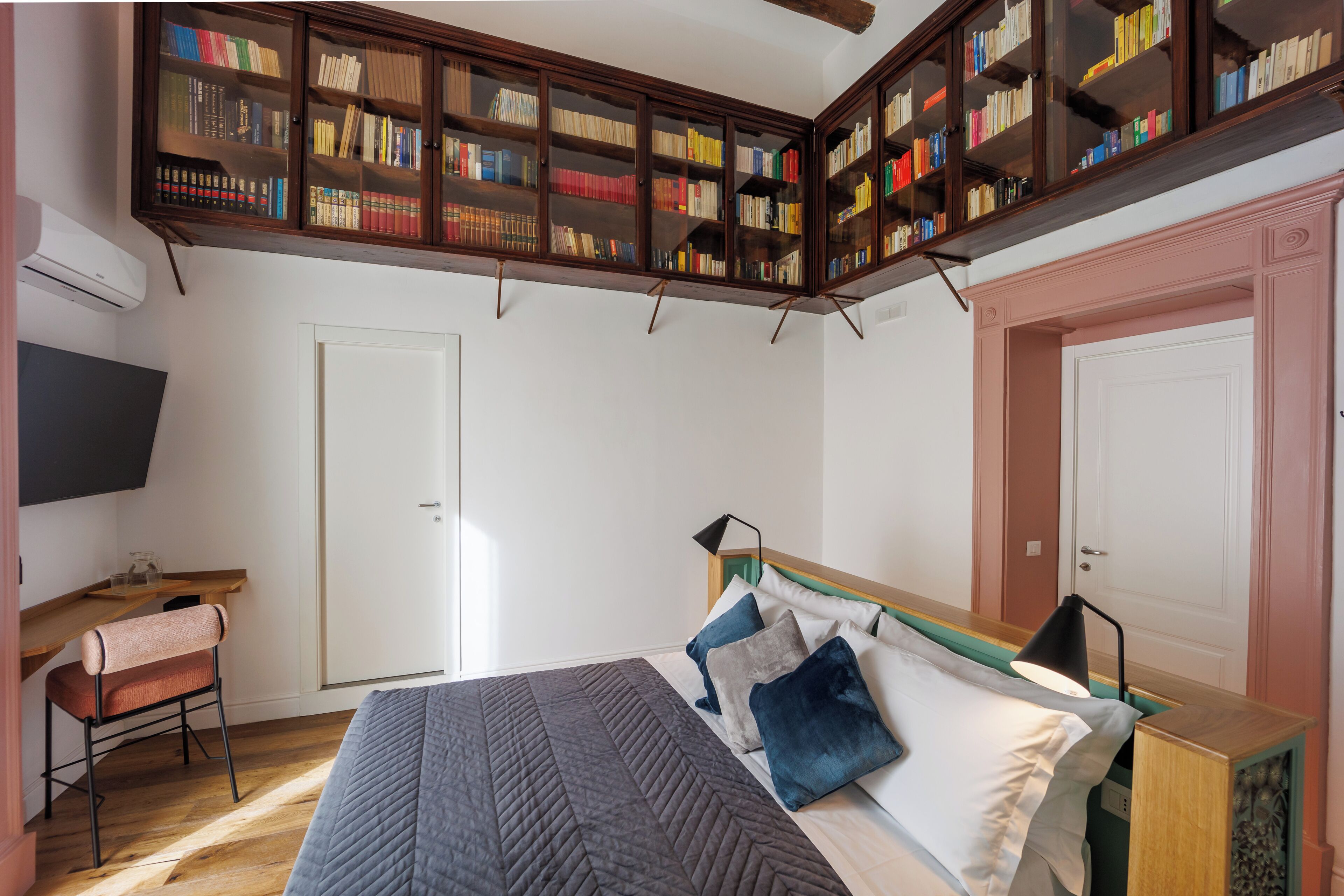 A bedroom with a bed, bedside table, lamp, chair, and a bookshelf.