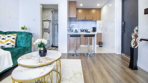 A compact living space with a green sofa, a marble coffee table, and a kitchen area with wooden cabinets and two bar stools. - Alba Garden (Nairobi)