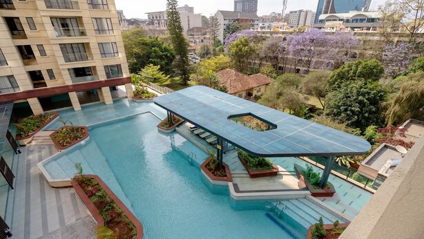 A rooftop pool with a glass canopy, surrounded by greenery and modern buildings in the background. - Alba Garden (Nairobi)