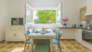 A compact kitchen with a dining area, a TV on a cabinet, and a window with a view of trees.