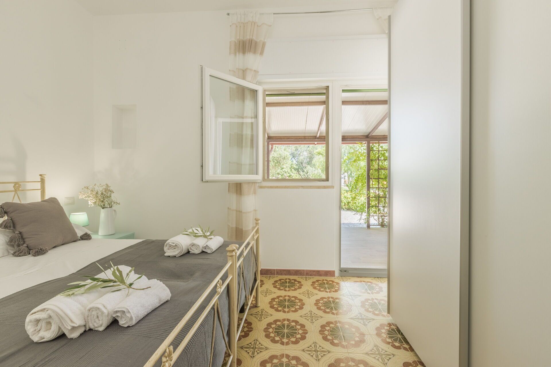 A bedroom with a bed, a nightstand, a window, and a view of the outdoors.