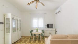 A room with a dining table, chairs, a sofa, a cabinet, a ceiling fan, a TV, and patterned flooring.