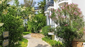 A pathway leading to a building with a stone wall, surrounded by lush greenery and flowering plants. - Ladonia Hotels Leo Beach Resort +16 (Bodrum)