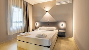 Une chambre d’hôtel moderne, dotée d’un grand lit, de tables de chevet, d’un luminaire fixé au mur et d’un appareil de climatisation.