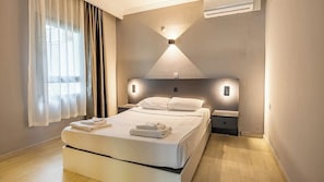 A modern hotel room with a large bed, bedside tables, a wall-mounted light fixture, and an air conditioning unit. - Ladonia Hotels Leo Beach Resort +16 (Bodrum)