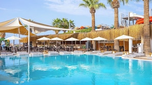 Un espace piscine aménagé avec des chaises longues et des parasols, des palmiers et un poste de surveillance pour les sauveteurs.