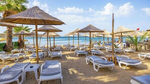 Une plage avec des chaises longues et des parasols en chaume.