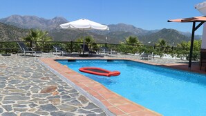 A swimming pool with a red float, surrounded by stone tiles and a wooden deck, with mountains in the background. - El Escalador - Detached finca in the mountains outside Competa (Cómpeta)