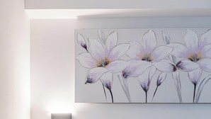 Una habitación de hotel con una cama, una mesita de noche, una lámpara en la pared y una obra de arte floral sobre la cama.