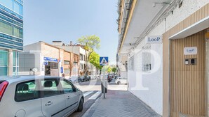 Una calle estrecha con un coche estacionado a la izquierda y un edificio con un cartel que dice 'LooP' a la derecha.
