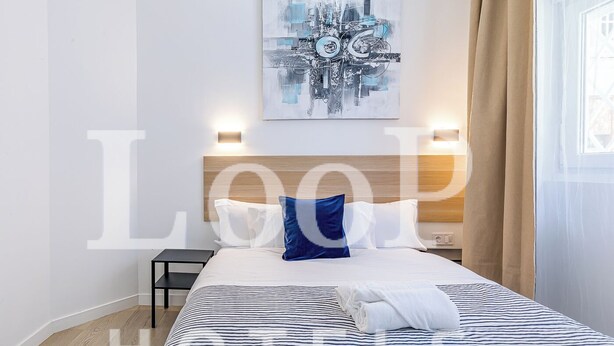 Habitación de hotel con cama, cabecera, una obra de arte en la pared y una ventana con cortinas.