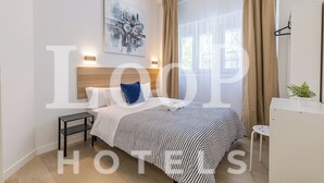 Una habitación de hotel con cama, mesitas de noche, una obra de arte en la pared y una ventana con cortinas.