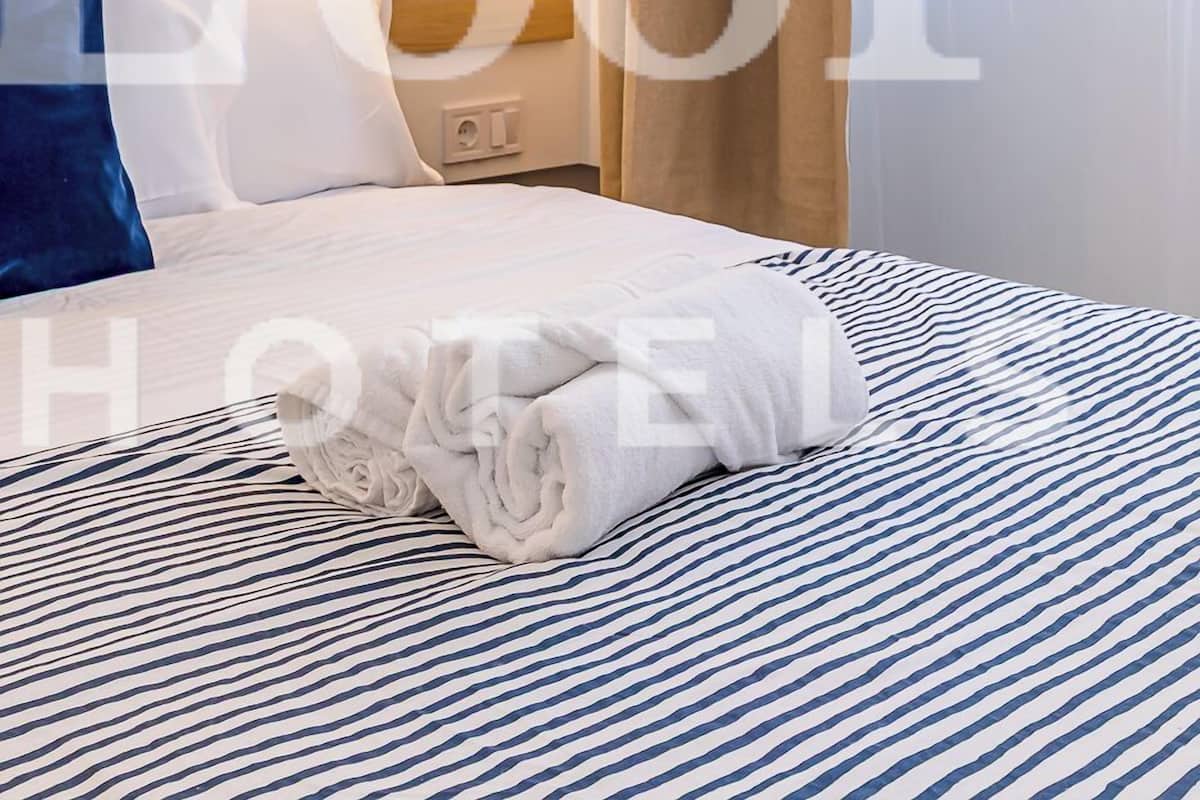 A hotel room with a neatly made bed, a headboard, a wall-mounted light, and a window with curtains.