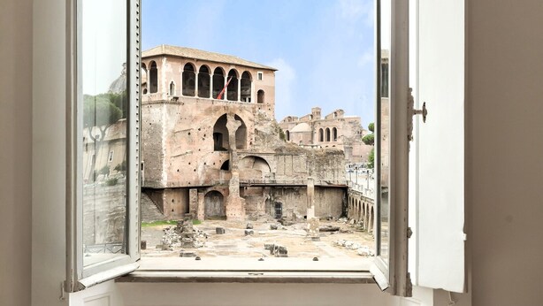 A view of ancient ruins through a window, including a large building with arches and a smaller structure in the background. - NEW overlooking ancient Rome (Roma)