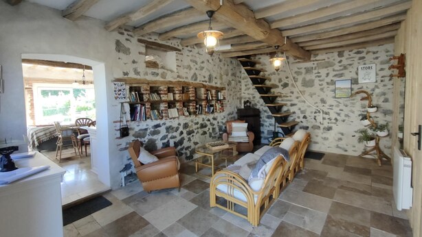 A rustic room with exposed brick walls, a wooden ceiling, a staircase, and a bookshelf filled with books. - La Source de nos Racines : Gîte de caractère (Beaufort)