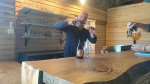 A wooden bar area with shelves of glasses and a bottle of beer on the counter. - La Source de nos Racines : Gîte de caractère (Beaufort)