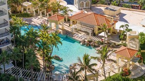 Ein Resort mit einem zentralen Pool, mehreren Liegebereichen und einem Gebäude mit einem Ziegeldach.
