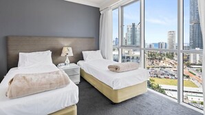 A hotel room with two beds, a nightstand, a lamp, and a large window offering a city view.
