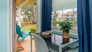 Un balcón con vistas a un barrio residencial, una silla, una mesita con libros y una planta en maceta.