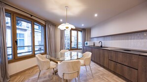 A modern kitchen with a glass dining table surrounded by chairs, wooden cabinets, and large windows with curtains. - Apartamento Turístico Royal (Cartagena)