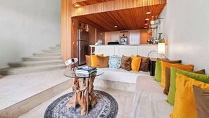 A modern interior with a wooden ceiling, a kitchen area, and a seating area with cushions.