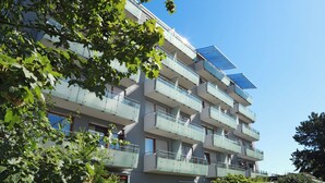 Un edificio residencial de varios pisos con balcones, un panel solar y vegetación circundante.