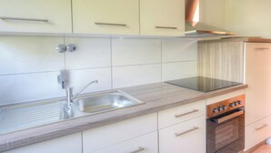 Una cocina con un lavamanos de acero inoxidable, horno empotrado y armarios de color claro.