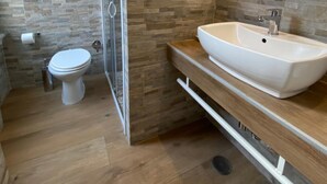 Et moderne badeværelse med et glasbrusekabine, en hvid vask og et toilet.