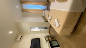 Habitación de hotel con cama, mesita de noche con lámpara, ventana con cortinas y aire acondicionado instalado en la pared.