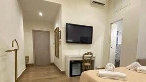 Una habitación de hotel con cama, escritorio, televisor y aire acondicionado.