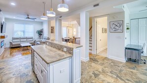 A spacious kitchen with a central island, pendant lighting, and a dining area with a staircase leading to another level.