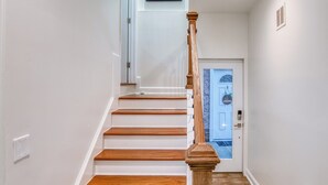A staircase with wooden steps and a wooden handrail, leading to a door with a light switch above it.