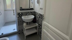 Een badkamer met een witte wasbak, een spiegel, een haardroger en een douche.