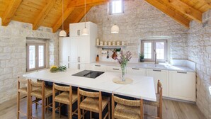 A spacious kitchen with a large island, stone walls, wooden beams, and white cabinetry. - Stone House Trogir - with jacuzzi (Trogir)