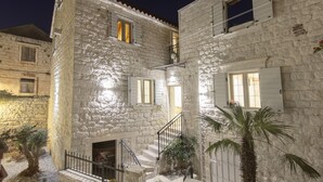 A stone building with a staircase leading to a door, surrounded by a small garden and palm trees. - Stone House Trogir - with jacuzzi (Trogir)