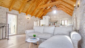 A spacious living area with a large grey sectional sofa, a small round table with a plant, and a stone wall. - Stone House Trogir - with jacuzzi (Trogir)