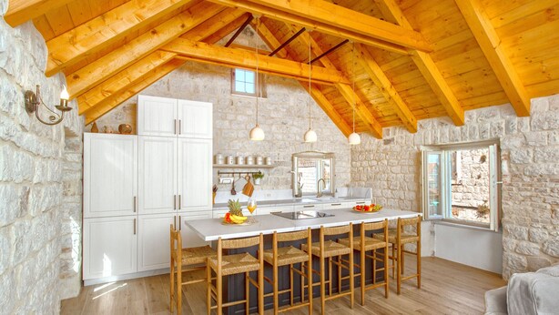 A rustic kitchen with stone walls, wooden beams, and a central island with bar stools. - Stone House Trogir - with jacuzzi (Trogir)