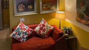 A room with a red sofa, two framed paintings, a lamp, and a poster on the wall. - Le Stanze dei Cardinali guest house c1 (ROMA)