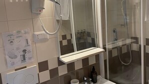 Un baño con un lavabo blanco, un espejo, cabina de ducha y un secador de pelo montado en la pared.