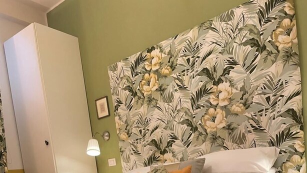 Een slaapkamer met een bed, een kledingkast, een bloemen behang en een lamp.