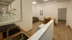 Eine moderne Küche mit Spüle aus Edelstahl, ein Essbereich mit Holztisch und Stühlen, eine Couch und ein gerahmtes Bild an der Wand.